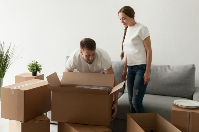 Stel pakt samen dozen in tijdens woning ontruimen, met kartonnen dozen en een bank op de achtergrond.