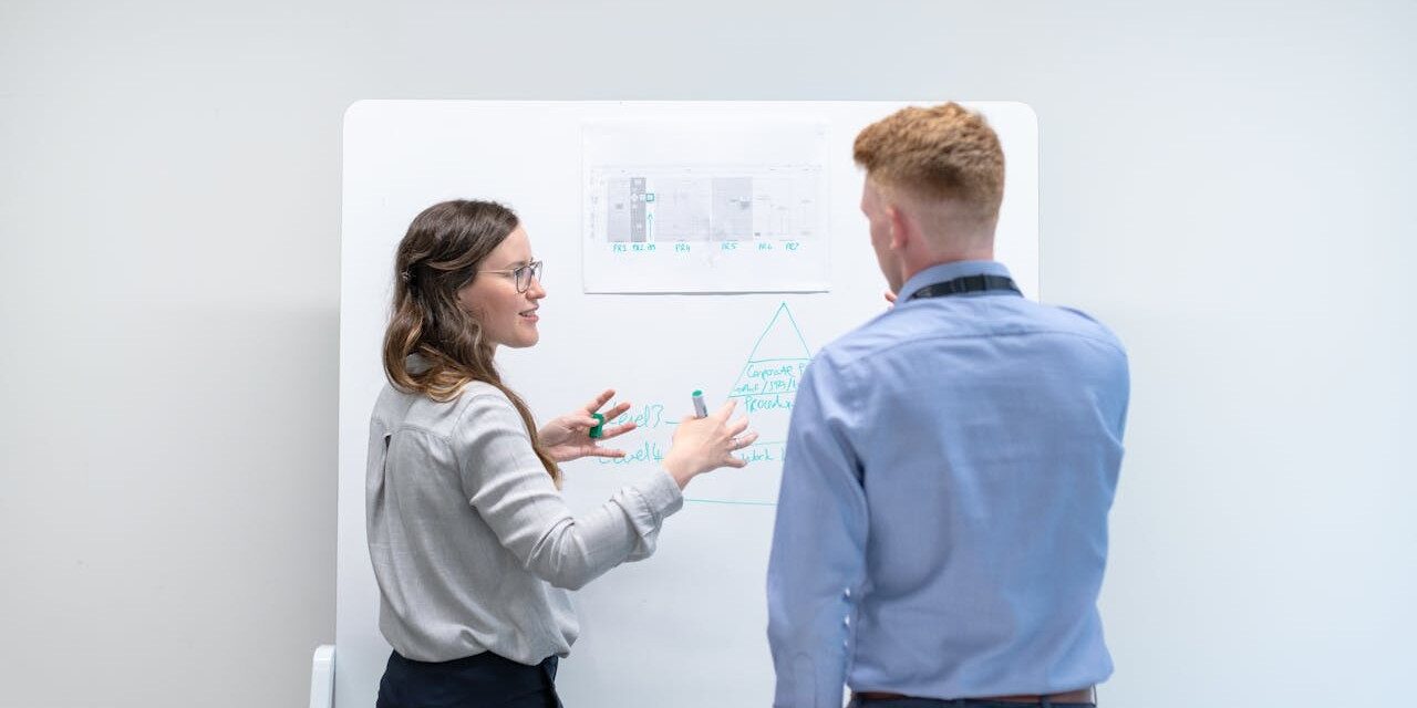 Twee collega's bespreken een technisch schema op een whiteboard tijdens een uitleg over een immersieve demo.